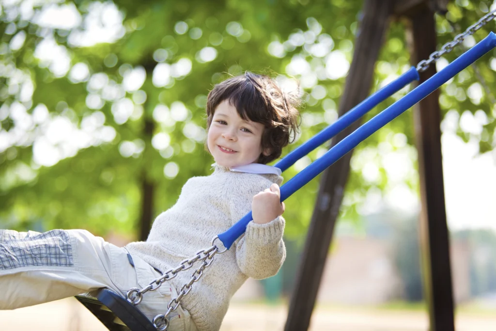 image of young boy swinging on a swing in a local park